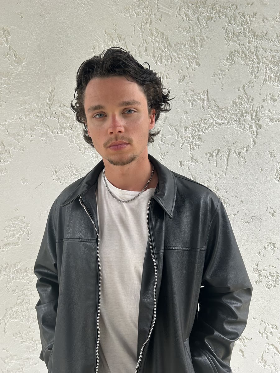 Angelo Guidet, en veste de cuir noire devant un mur blanc