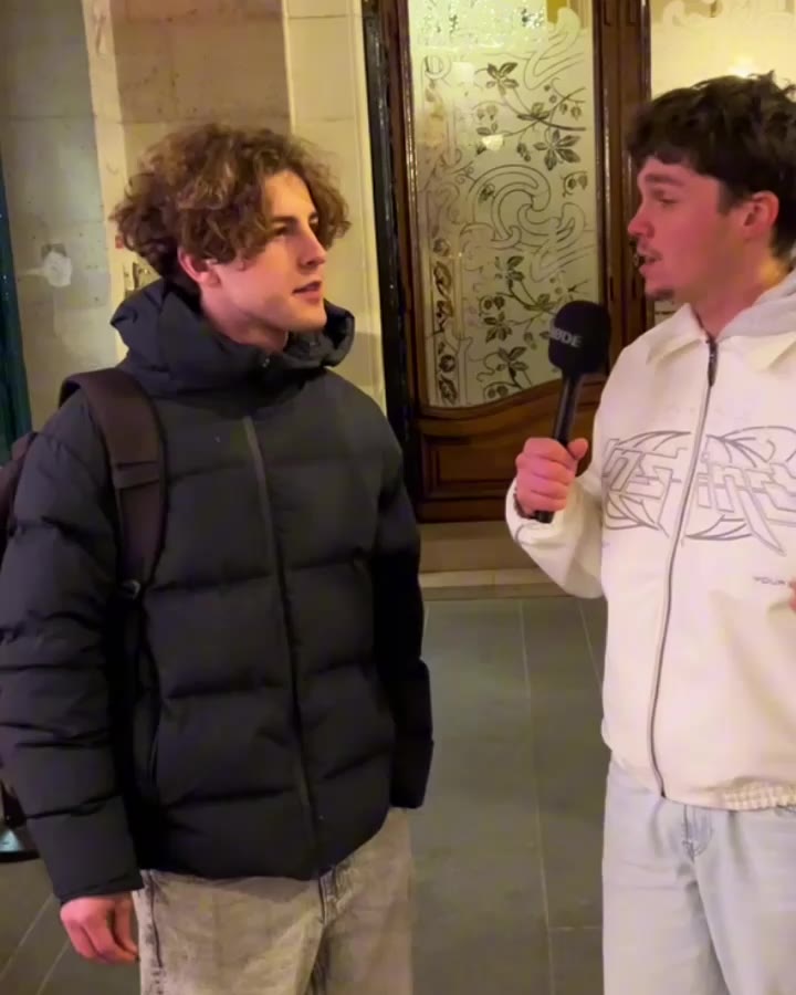 Angelo, en blanc, micro à la main, interroge un passant pendant un micro-trottoir